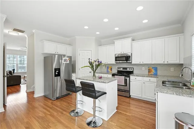 a kitchen with stainless steel appliances kitchen island granite countertop a refrigerator a stove top oven a sink dishwasher and white cabinets with wooden floor