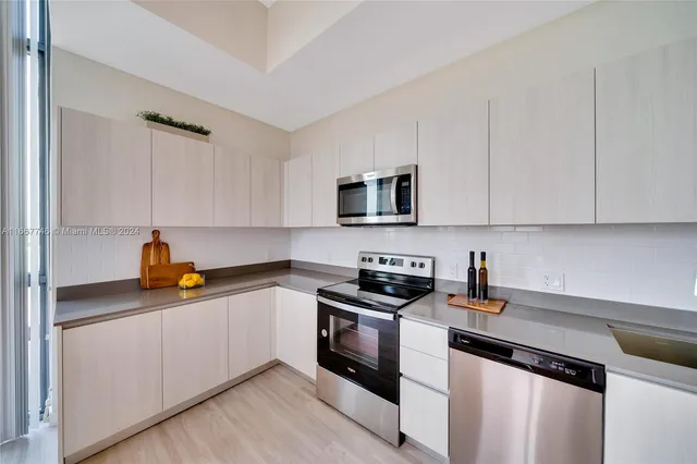 a kitchen with stainless steel appliances a sink dishwasher a refrigerator a stove and white cabinets with wooden floor