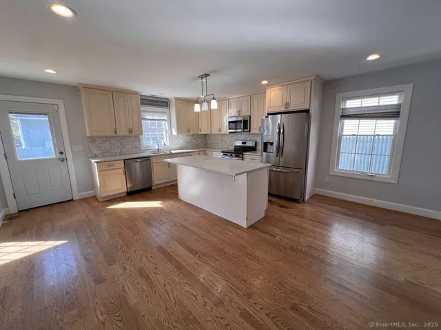 a kitchen with stainless steel appliances a stove top oven a sink a refrigerator with wooden floors and cabinets