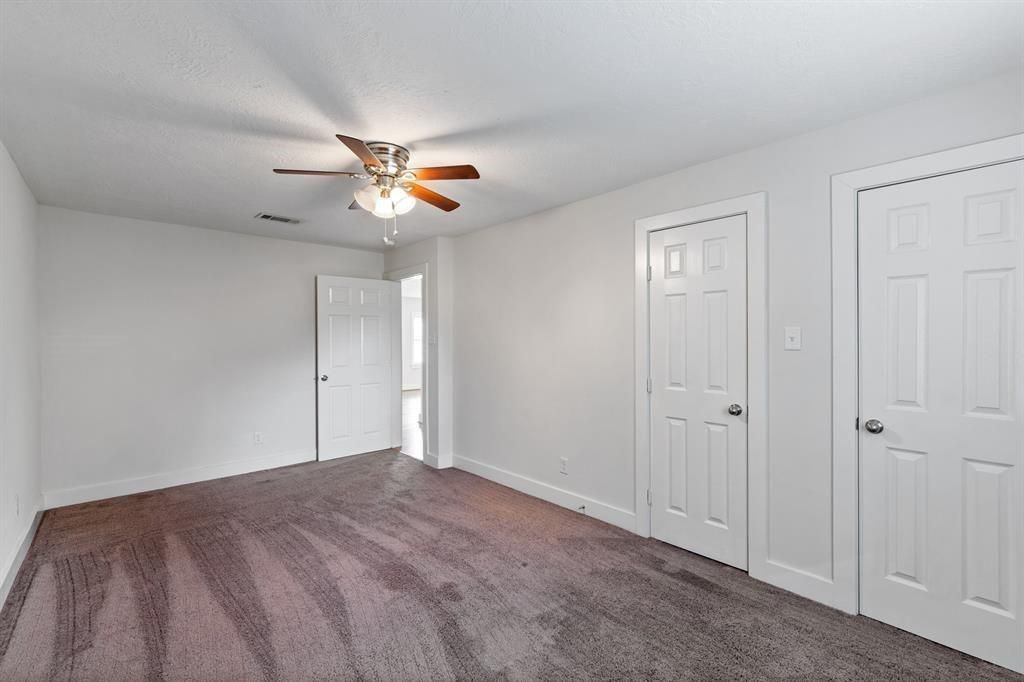 1305 Idylwild Street Houston, TX 77009 - Photo 14 of 31 This photo shows a spacious, carpeted bedroom with neutral walls, a ceiling fan, and two closed doors, likely for closets or additional rooms. A third door leads to another area. The room is well-lit, offering a cozy and functional space.