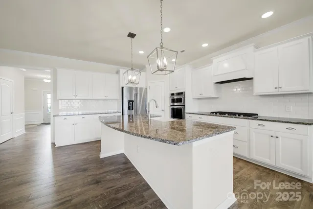 a large kitchen with granite countertop a white stove top oven a sink dishwasher and a refrigerator with wooden floor