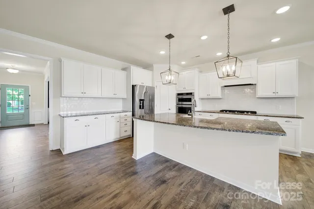 a large kitchen with stainless steel appliances kitchen island a refrigerator a sink dishwasher a stove and white cabinets with wooden floor