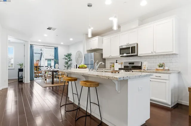 a kitchen with stainless steel appliances granite countertop a refrigerator a stove top oven a sink dishwasher and white cabinets with wooden floor
