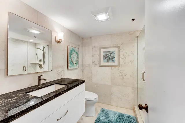 a bathroom with a granite countertop sink a toilet a mirror and shower