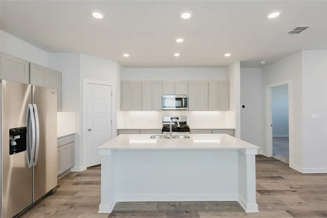 a large white kitchen with kitchen island a refrigerator a sink and white cabinets