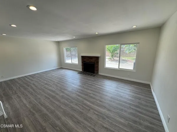 an empty room with wooden floor fireplace and windows
