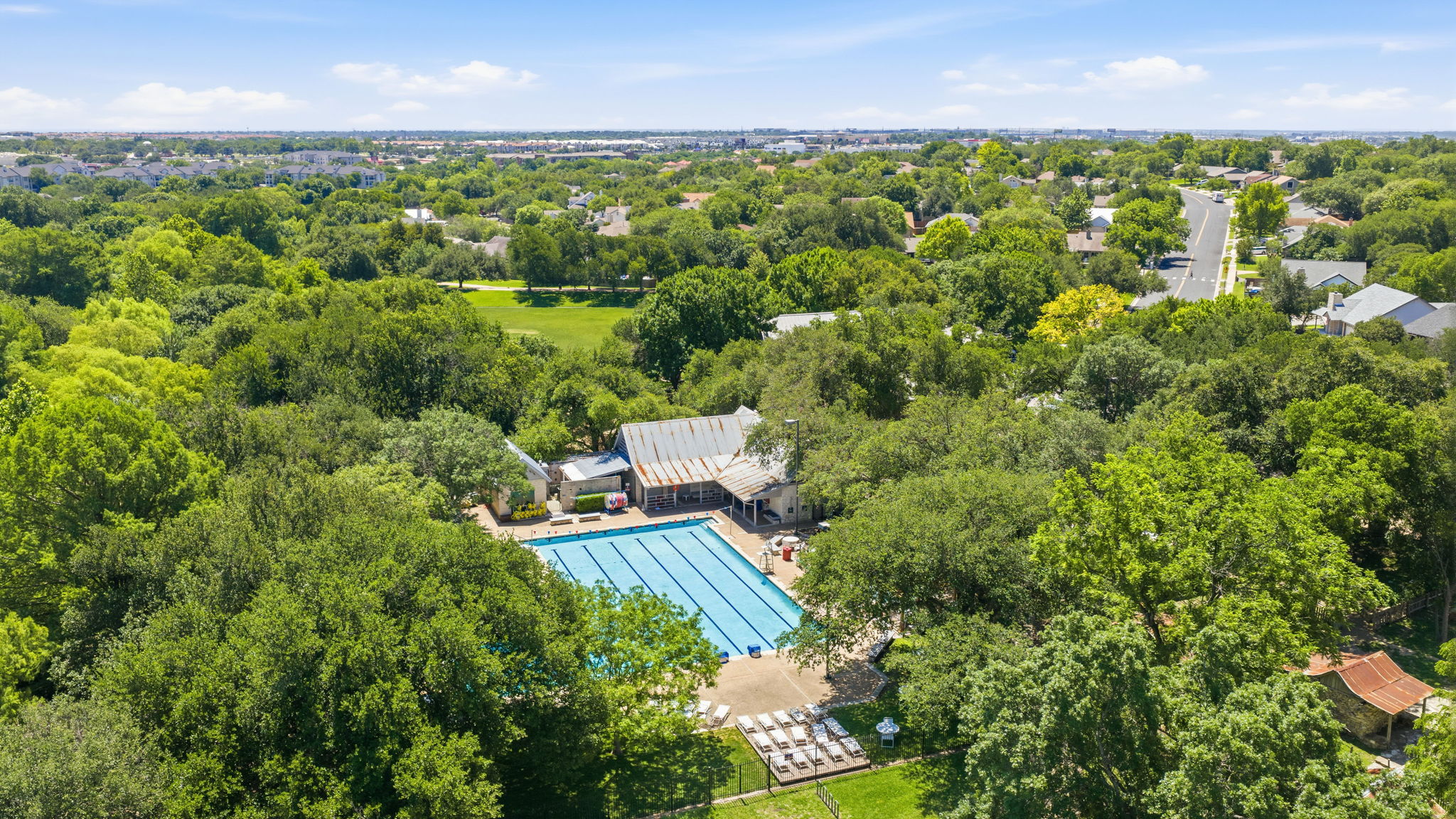 14818 Yellowleaf Trail Austin, TX 78728 - Photo 25 of 26 Outdoor swimming pool surrounded by mature trees, featuring a paved deck with lounge chairs and a building with a corrugated metal roof
