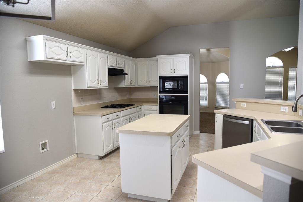 1526 Pebblestone Court Allen, TX 75002 - Photo 5 of 28 Kitchen featuring a vaulted ceiling, white cabinetry with decorative panels, stainless steel dishwasher, double basin sink, and a central island