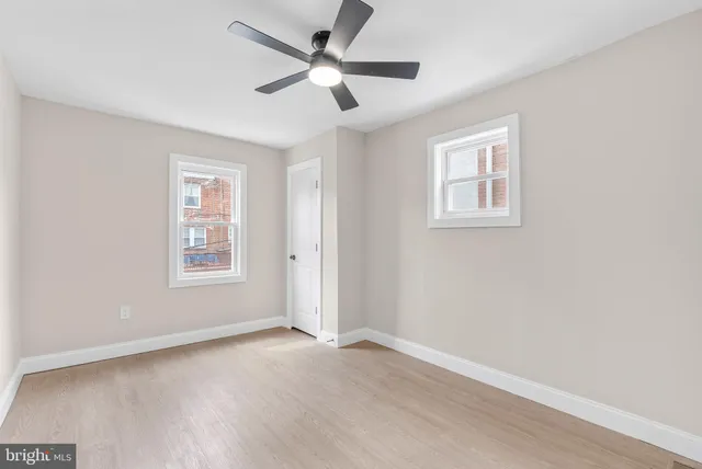 an empty room with wooden floor ceiling fan and windows