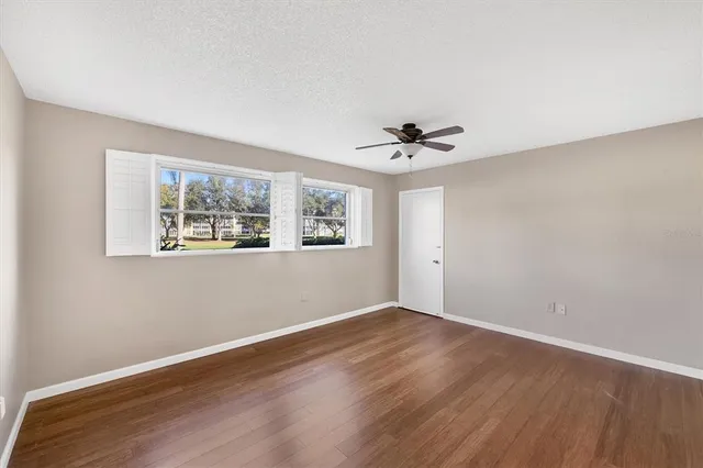 a view of an empty room with wooden floor and a ceiling fan