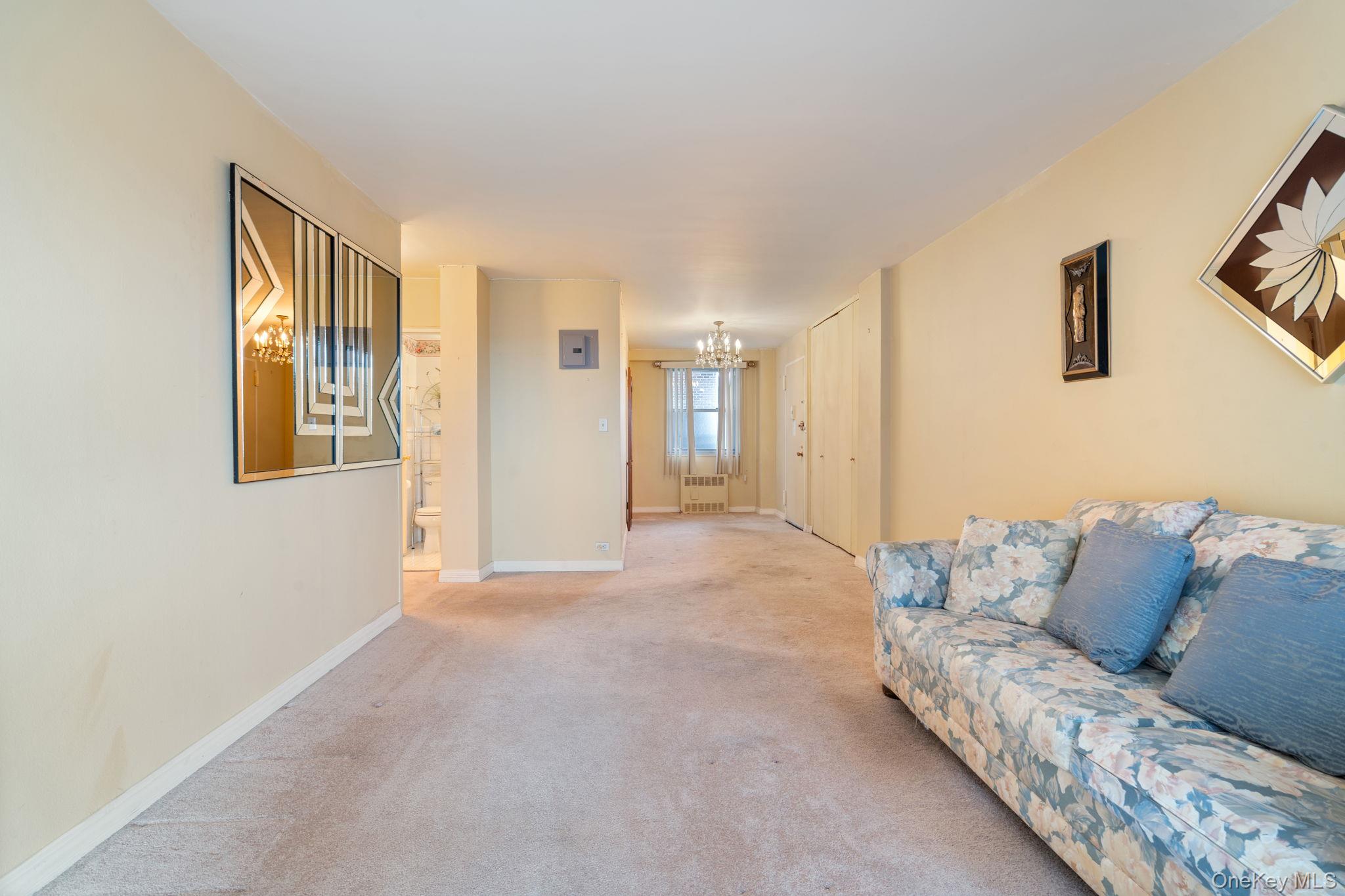61-15 97th Street, Unit 12H Queens, NY 11374 - Photo 7 of 23 Carpeted living room featuring a chandelier and radiator heating unit
