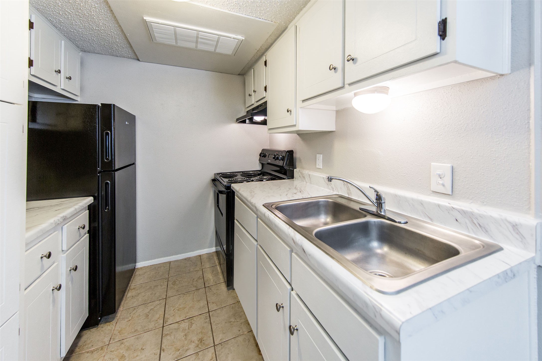 108 West 45th Street, Unit 110 Austin, TX 78751 - Photo 5 of 7 Kitchen with black appliances, light countertops, white cabinets, light tile patterned flooring, and under cabinet range hood
