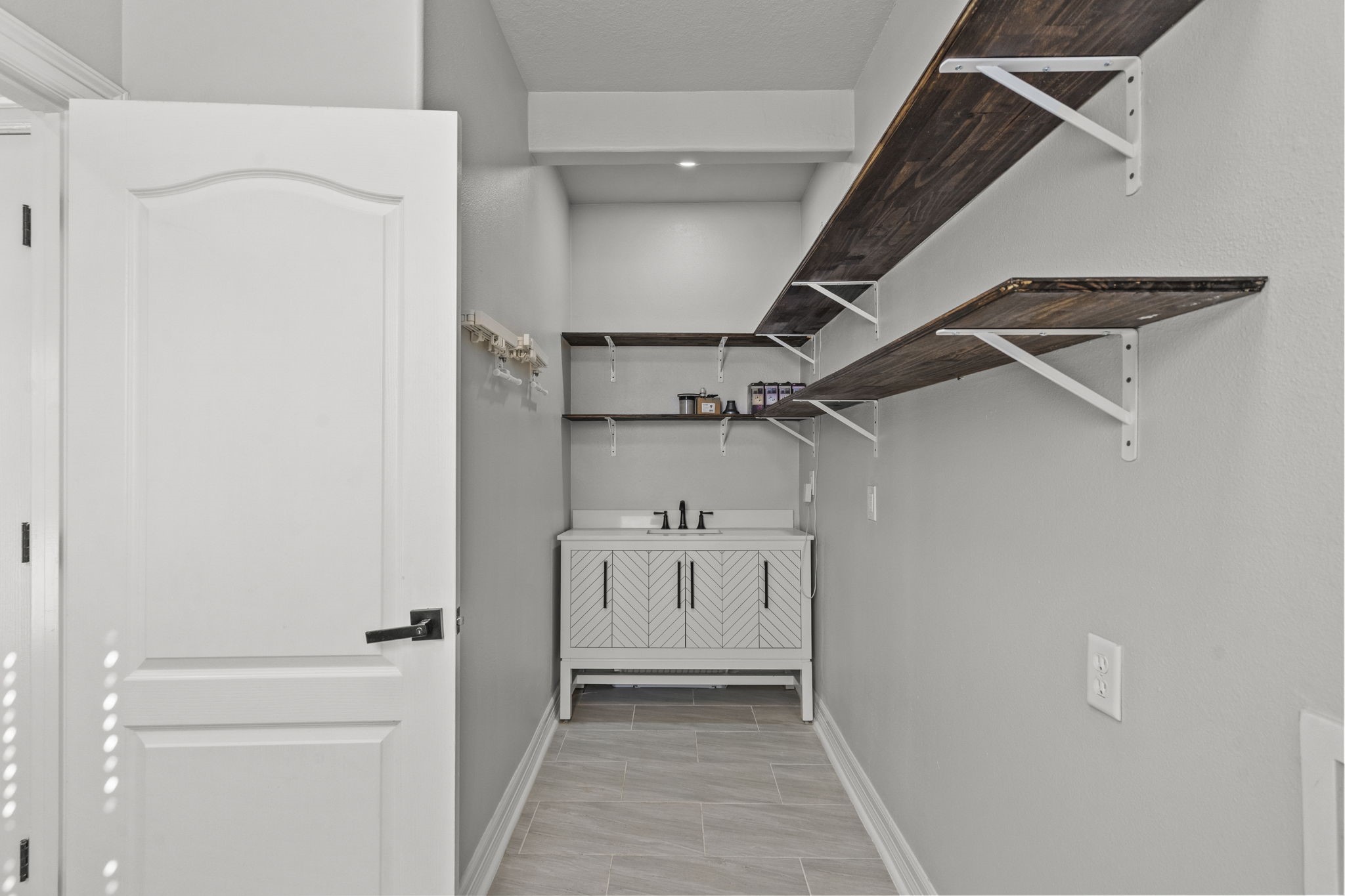 2730 Lawrence Road Kemah, TX 77565 - Photo 19 of 46 This photo showcases a modern laundry room with light gray walls, featuring a sleek cabinet with a sink, open dark wood shelving, and ample storage space.
