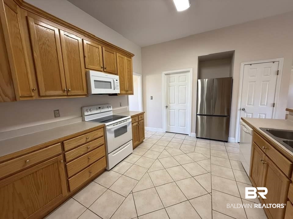 10428 South Side Loop Fairhope, AL 36532 - Photo 14 of 28 Kitchen featuring brown cabinets, light countertops, light tile patterned flooring, white appliances, and baseboards