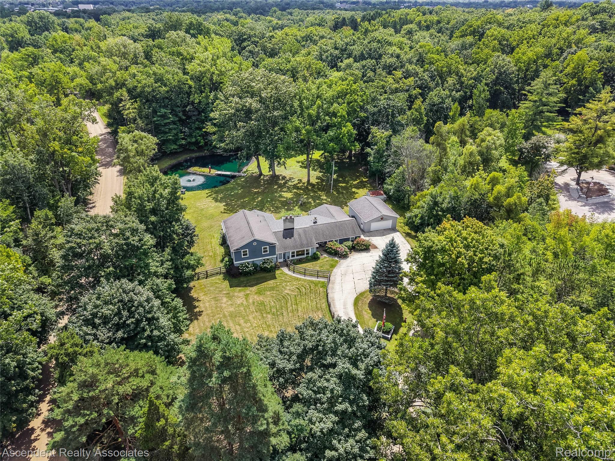 6157 Blue Beech Court Rochester, MI 48306 - Photo 26 of 30 Expansive property surrounded by mature trees, featuring a private pond with a fountain and dock, a detached garage, and a circular driveway