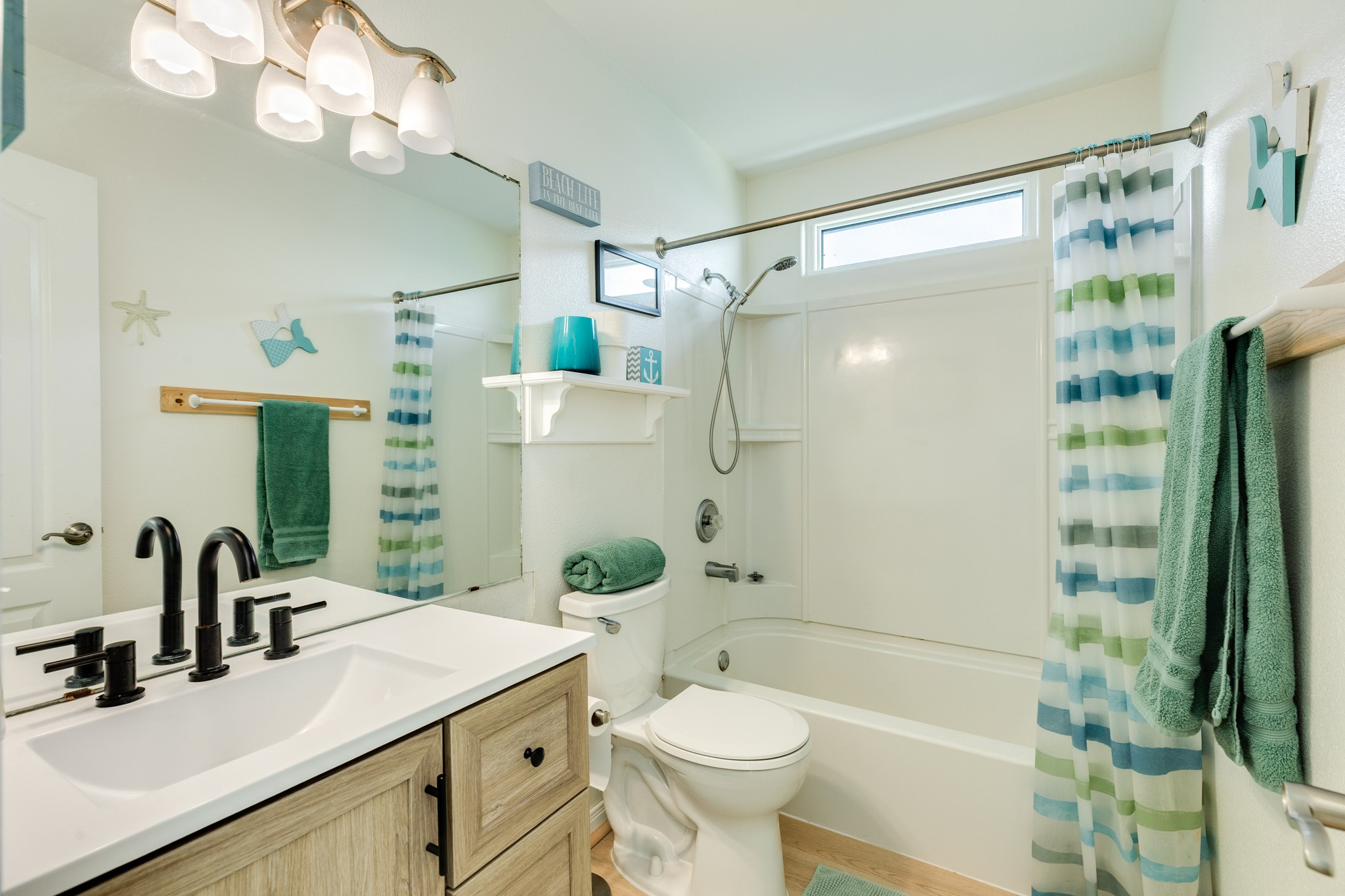 210 Beach Drive Surfside Beach, TX 77541 - Photo 29 of 33 Hall Bathroom – Fresh, coastal bath with modern vanity and matte-black fixtures, plus a tub/shower combo with handheld sprayer and transom window.