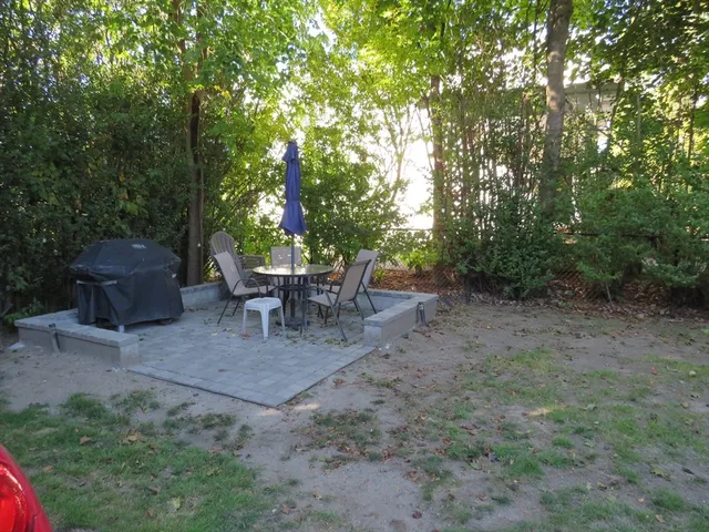 a view of a backyard with table and chairs potted plants and large tree