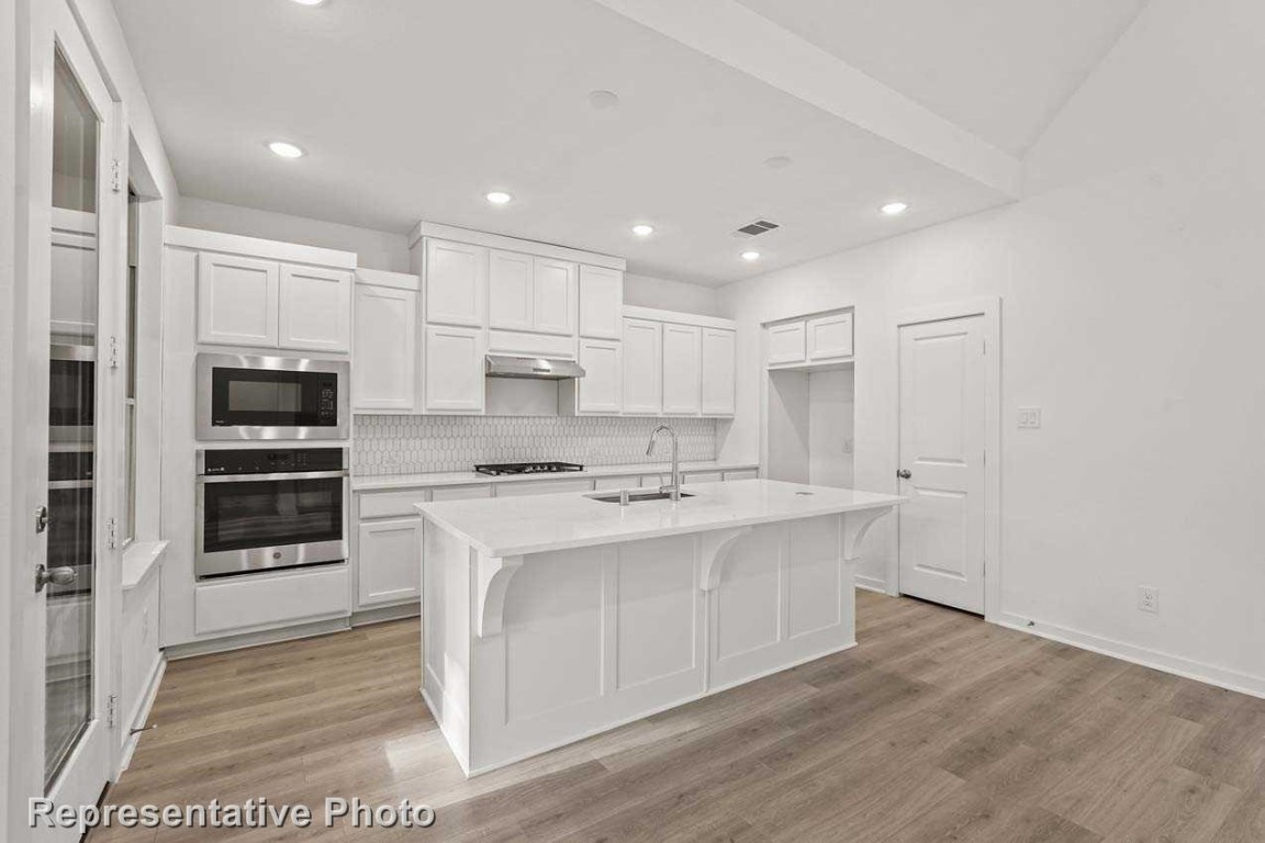 a large kitchen with kitchen island a sink a stove a refrigerator and white cabinets