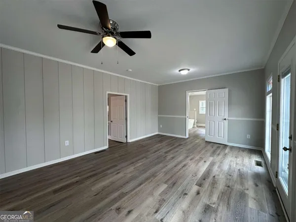 a view of an empty room with wooden floor and a ceiling fan