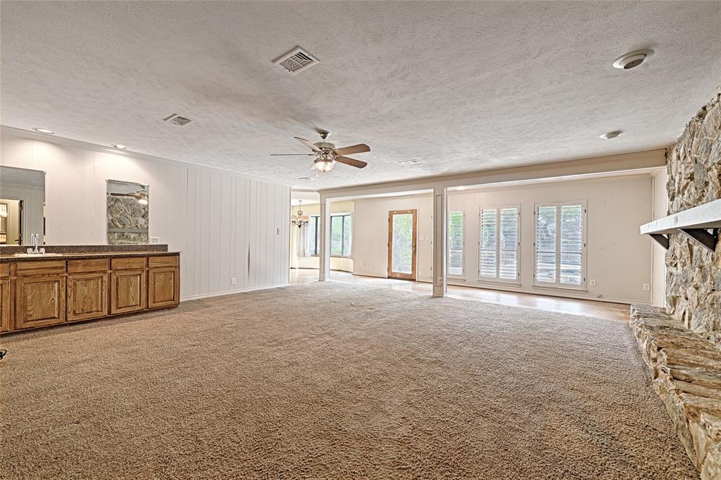 3004 Wingren Road Irving, TX 75062 - Photo 9 of 18 Spacious room featuring carpet flooring, a stone-clad fireplace with a mantel, built-in cabinetry with a countertop and mirror, multiple windows with plantation shutters, and recessed lighting