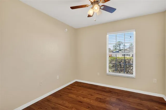 an empty room with wooden floor chandelier fan and windows