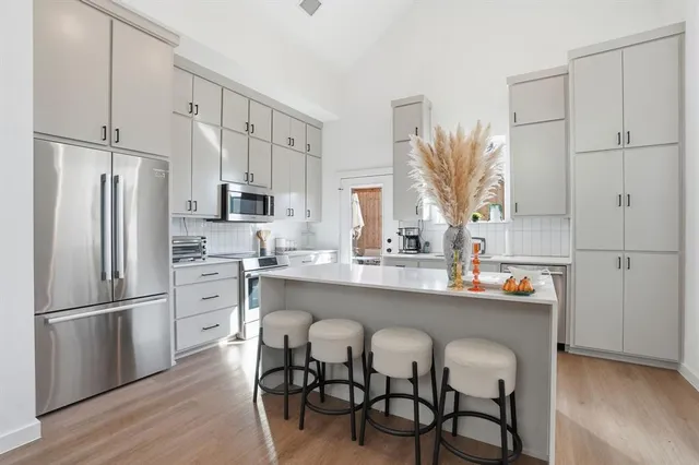 a kitchen with stainless steel appliances a refrigerator a sink dishwasher a stove and white cabinets with wooden floor