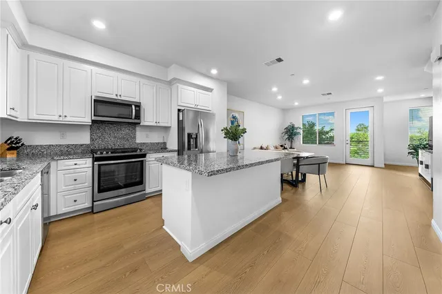 a kitchen with stainless steel appliances granite countertop a stove top oven a sink dishwasher a refrigerator and a dining table with wooden floor