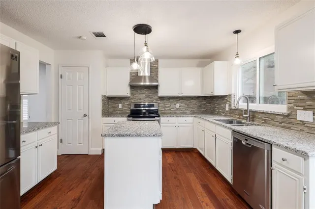 a kitchen with stainless steel appliances granite countertop a sink stove and white cabinets with wooden floor