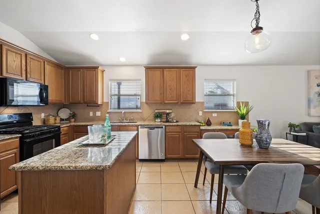 a kitchen with stainless steel appliances granite countertop a stove top oven a sink dishwasher and a refrigerator with wooden cabinets