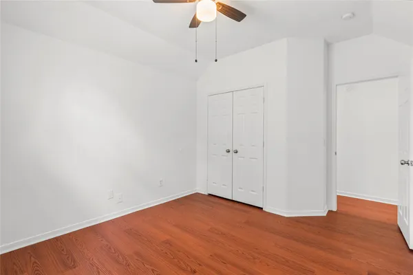 a view of an empty room with wooden floor ceiling fan
