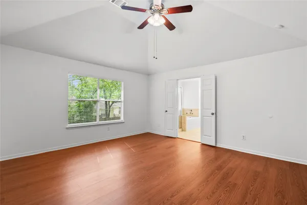 an empty room with wooden floor chandelier fan and windows
