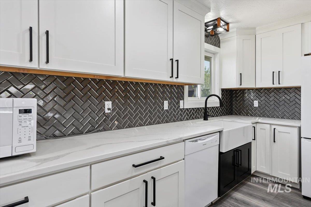 616 Doris Avenue Paul, ID 83347 - Photo 17 of 38 Kitchen featuring white appliances, white cabinets, decorative backsplash, light stone countertops, and wood finished floors