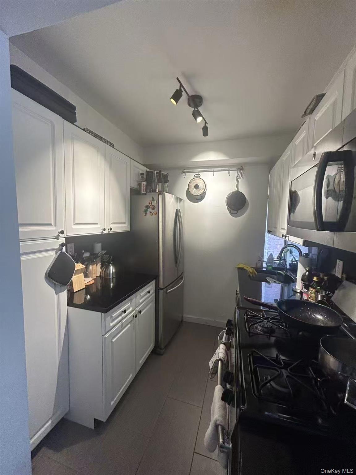 310 Lexington Avenue, Unit 5A Manhattan, NY 10016 - Photo 4 of 9 Kitchen with appliances with stainless steel finishes, white cabinets, a sink, track lighting, and dark countertops