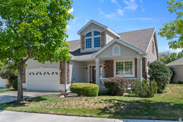 1417 Blacksmith Lane Draper, UT 84020 - Photo 1 of 57 Stucco facade residence featuring a covered front porch with white railing, stone accents, arched upper window with shutters, and an attached two-car garage with decorative window inserts