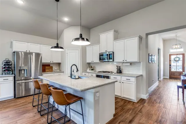 a kitchen with stainless steel appliances granite countertop a stove top oven a refrigerator a sink and a dining table with wooden floor