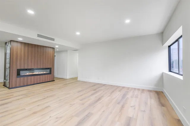 a view of empty room with wooden floor and kitchen