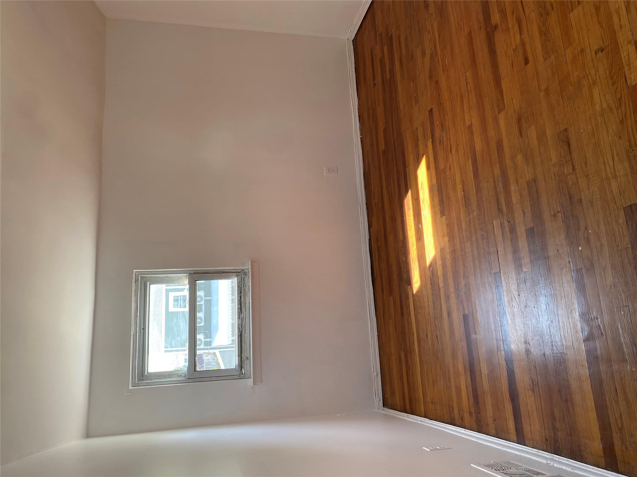 129-32 145th Street Queens, NY 11436 - Photo 8 of 15 a view of empty room with wooden floor and a window