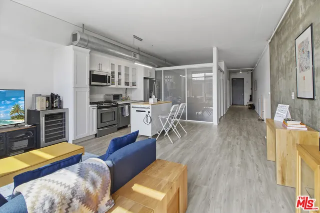 a living room with stainless steel appliances furniture a flat screen tv and kitchen view