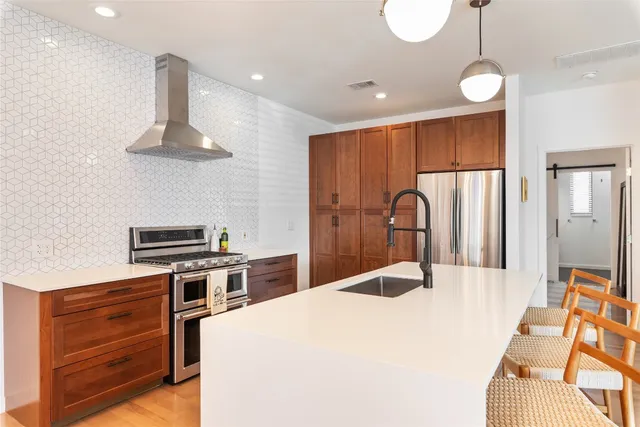 a kitchen with stainless steel appliances a stove a refrigerator oven a kitchen island with wooden floor and cabinets