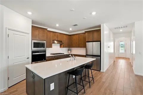 a kitchen with stainless steel appliances kitchen island granite countertop a refrigerator a sink dishwasher and a stove with wooden floor