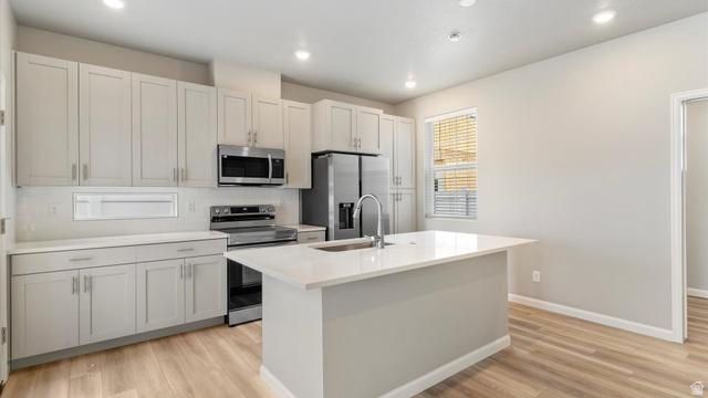 82 Provo River Road, Unit 251 Saratoga Springs, UT 84045 - Photo 9 of 32 Modern kitchen featuring light gray cabinetry, stainless steel appliances, a center island with an undermount sink, recessed lighting, and wood-finish flooring