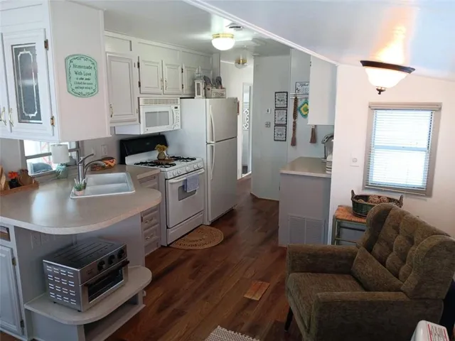 a living room with stainless steel appliances furniture a fireplace and a kitchen view