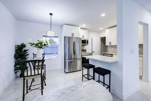 a kitchen with stainless steel appliances a refrigerator a stove a dining table chairs and white cabinets