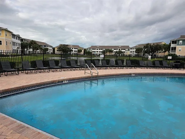 a swimming pool that has lawn chairs and a dining table under an umbrella