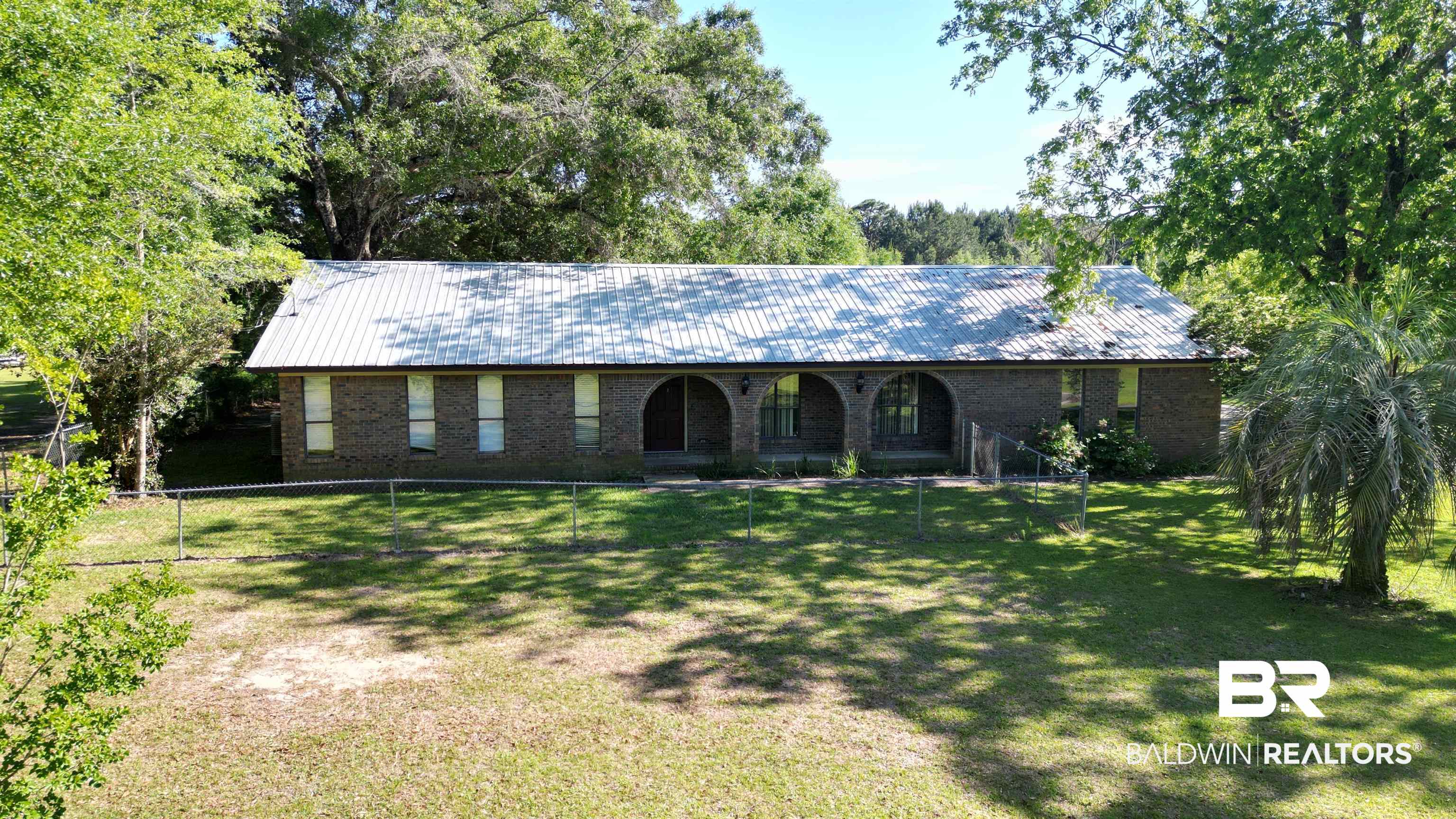33370 Highway 98 Lillian, AL 36549 - Photo 1 of 58 Brick exterior residence featuring a metal roof, arched front entryways, and mature perimeter trees