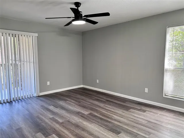an empty room with wooden floor fan and windows