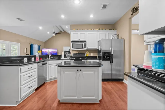 a kitchen with stainless steel appliances granite countertop a stove top oven a sink dishwasher a refrigerator and a dining table with wooden floor