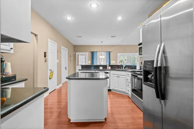 a kitchen with stainless steel appliances granite countertop a refrigerator a sink dishwasher a stove and white cabinets with wooden floor