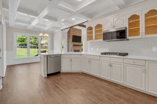 a large white kitchen with stainless steel appliances granite countertop a stove a sink and white cabinets with wooden floor
