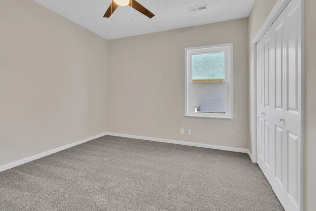 an empty room with chandelier fan and windows